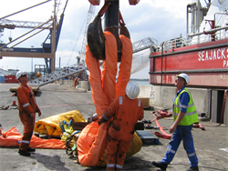 Some riggers placing a large orange textile sling onto a steel hook for use offshore