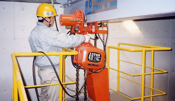 A orange hoist being worked on a girder